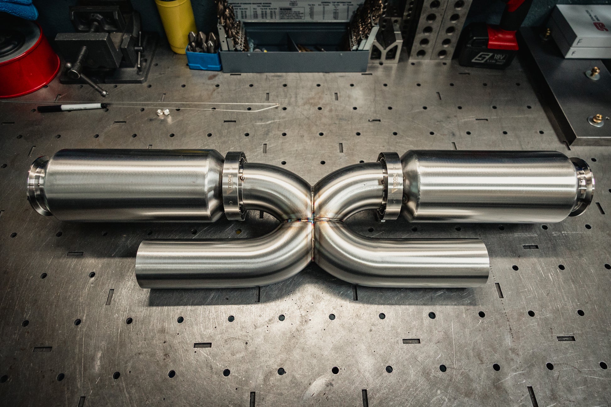 Metallic exhaust pipes on a workshop table with tools in the background